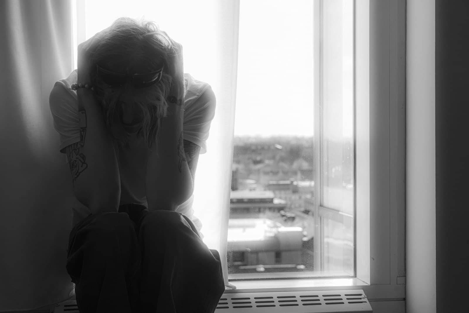 Person sitting alone by a window with their head in their hands